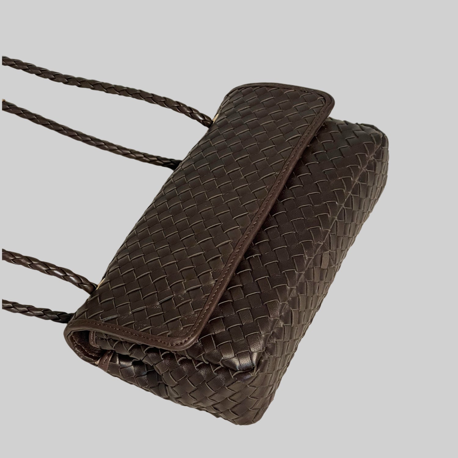 Ribichini Envelope-clutchen i sjokoladebrunt lammeskinn med gull-detaljer. Den justerbare hanken gir fleksibel bærestil, klaffen sikrer trygg oppbevaring.