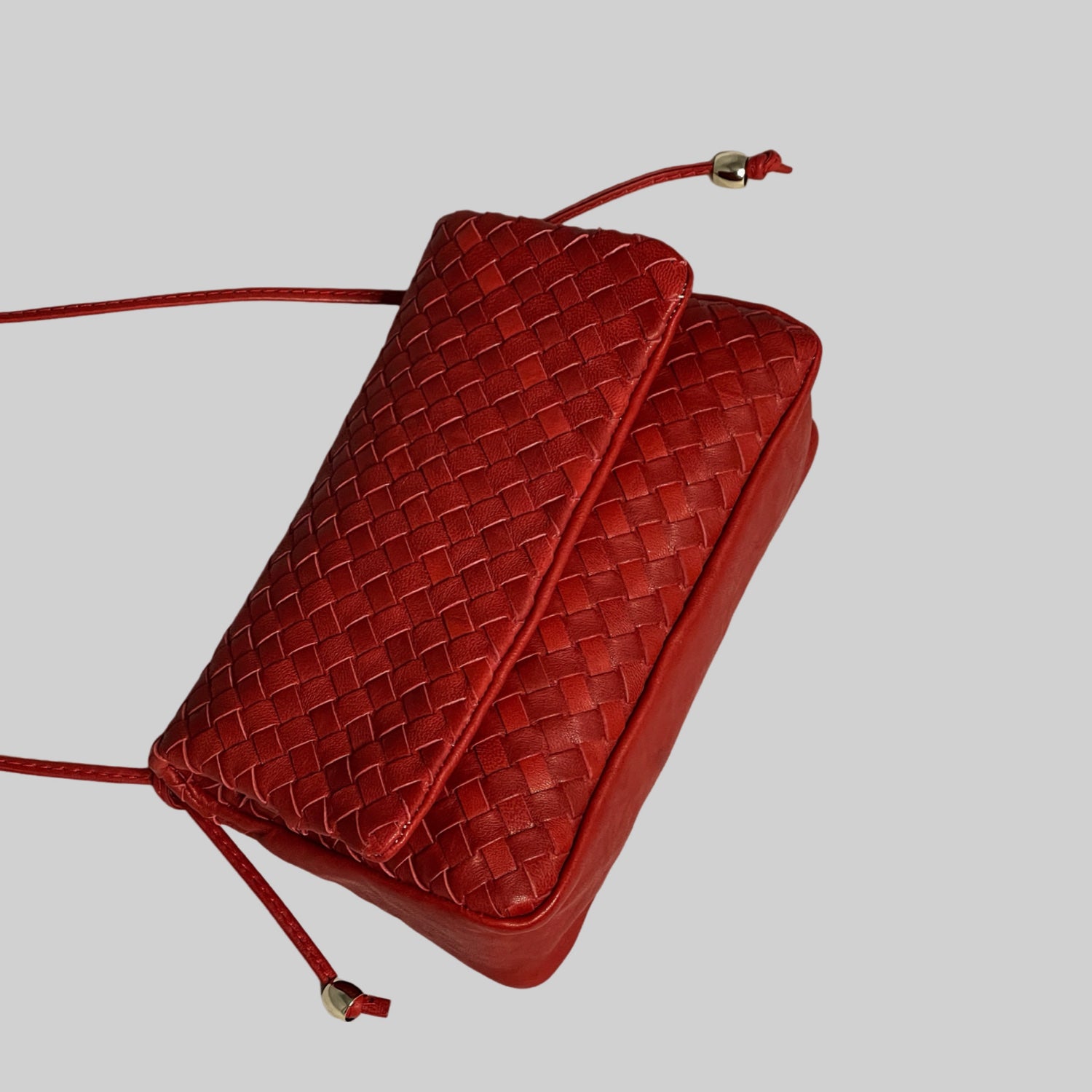 Ribichini Undercover i rødt: Praktisk, elegant flettet skinnveske. Magneter for sikker lukking. Stilige gulldetaljer. Praktisk og elegant.