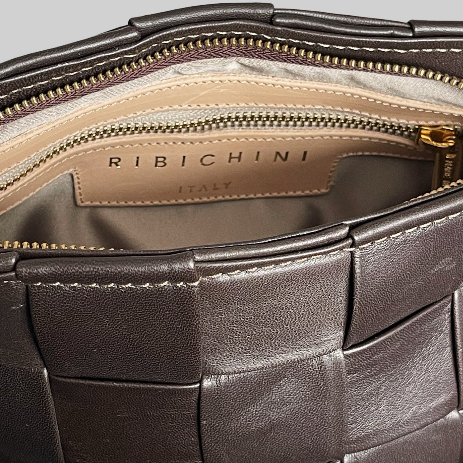 Innsiden av Ribichini Square Clutch i fargen chocolate viser etiketten "RIBICHINI ITALY" i gullskrift på en lys bakgrunn. Elegant kontrast og høykvalitets håndverk.