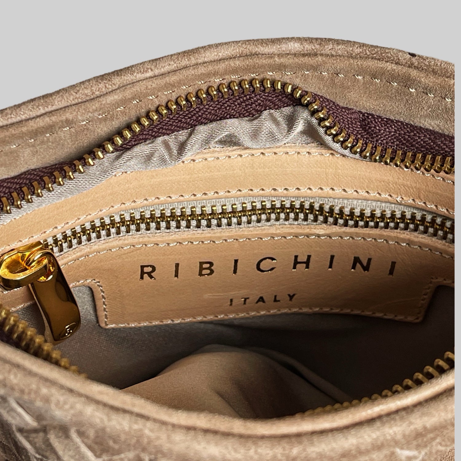 Nærbilde av innsiden av Ribichini Camper clutch i terra semsket lammeskinn med gulldetaljer og glidelås, merket "RIBICHINI ITALY".