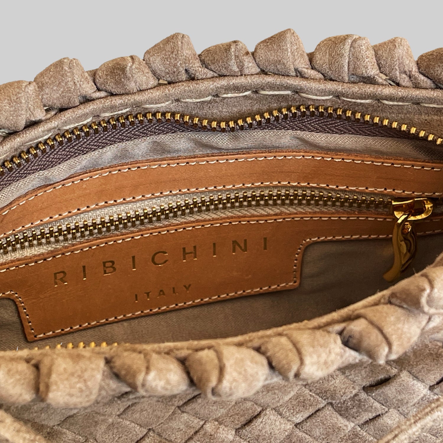 Nærbilde av innsiden på Ribichini Woodstock Royal clutch i terra semsket skinn, med gullglidelås og skinnmerke "Ribichini Italy".