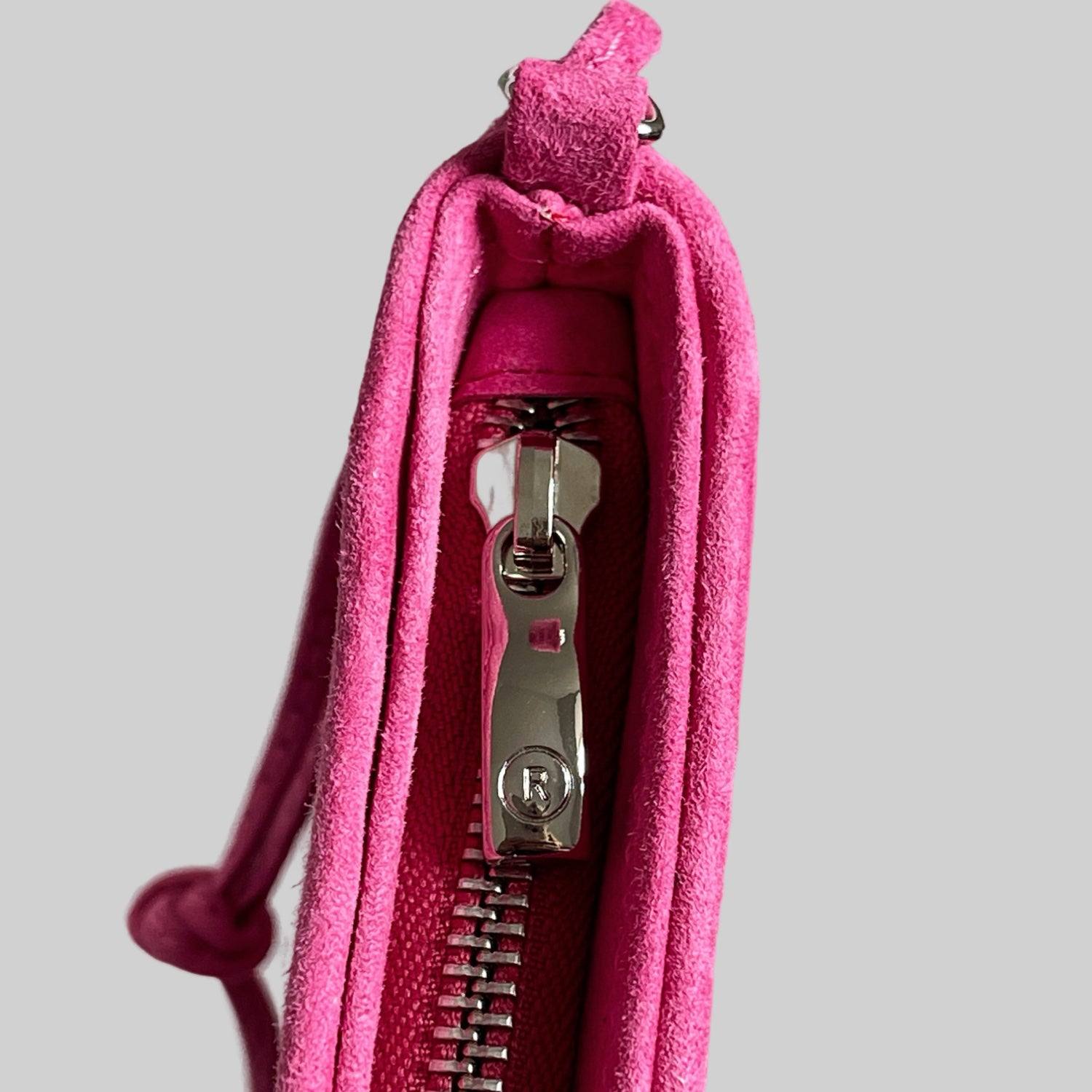 Detaljbilde av sølvglidelås med preget R-logo på rosa Ribichini clutch i semsket lammeskinn.