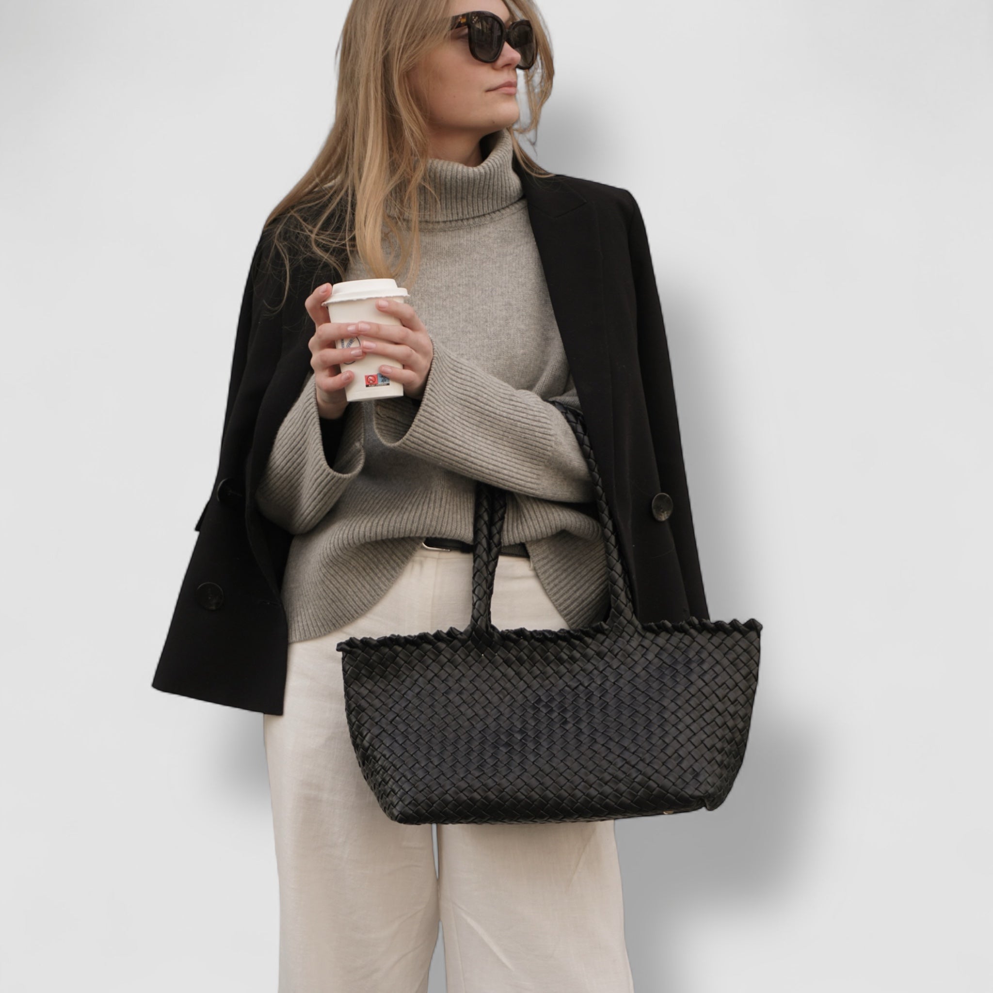 Kvinne med Ribichini Woodstock Classic Babe veske i sort flettet skinn, stylet med blazer og høyhalset genser.