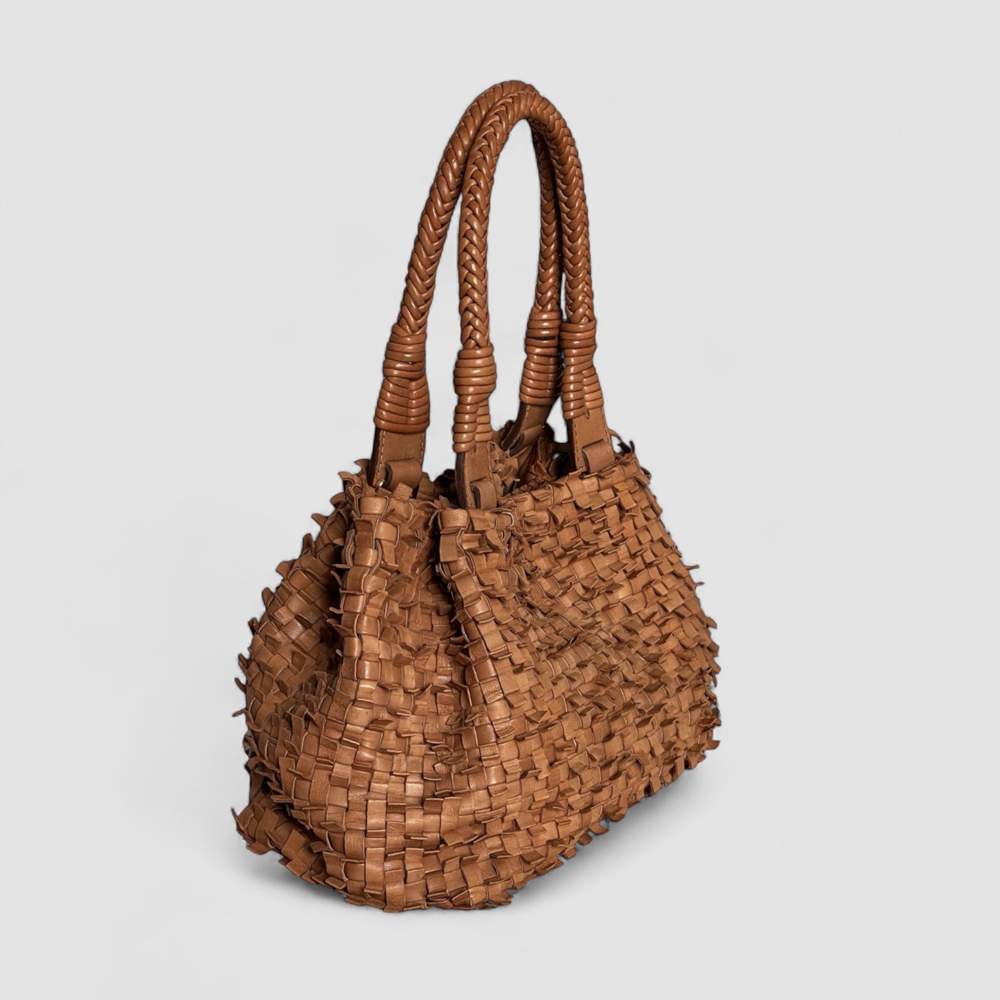  Ribichini Loren-vesken i cognac, håndlaget i plissért skinn med flettede håndtak og et unikt, strukturert design sett fra siden.