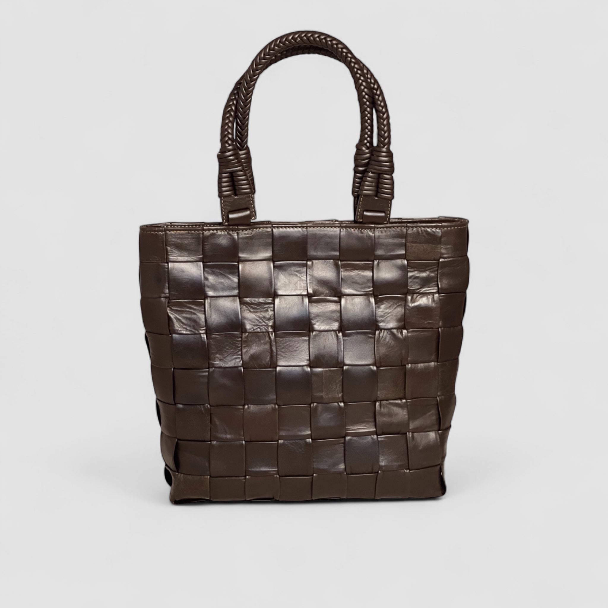 Ribichini Square Babe i fargen chocolate er en eksklusiv veske laget av håndflettet lammeskinn. Med store, generøse ruter og flettede hanker.