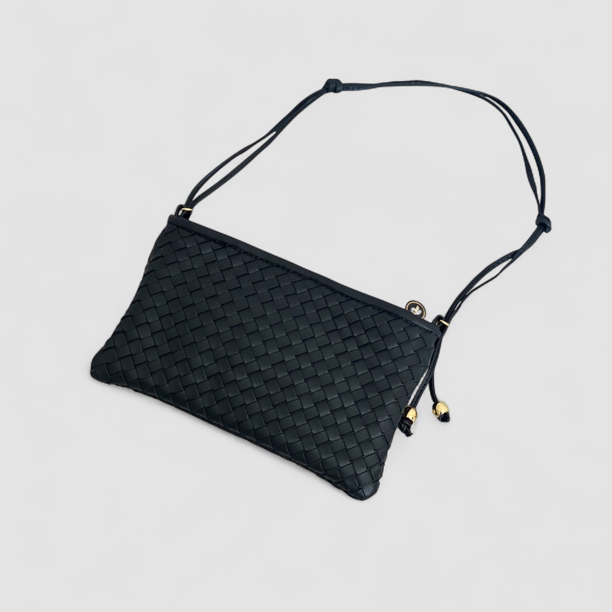 Ribichini Camper Clean-clutchen i sort liggende. Laget av flettet lammeskinn, med synlige gulldetaljer, gir den et luksuriøst preg.