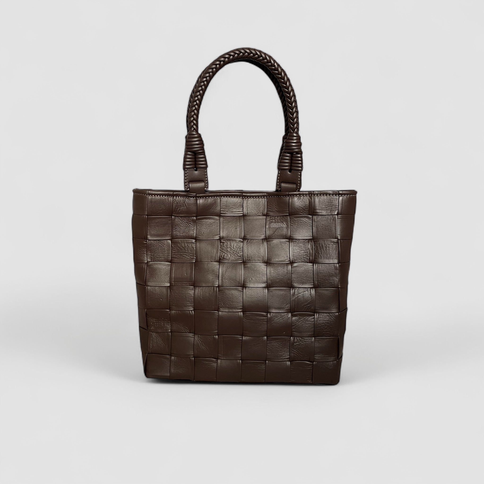 Ribichini Square Babe i fargen chocolate er en eksklusiv veske laget av håndflettet lammeskinn. Med store, generøse ruter og flettede hanker.