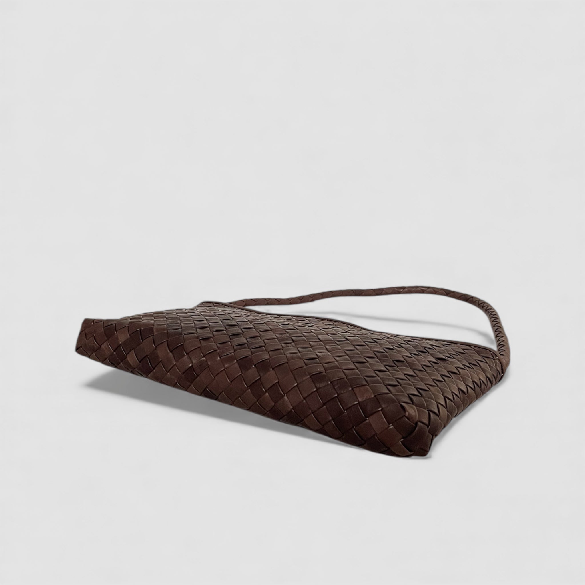 Brun Ribichini Classica i håndflettet skinn, vist nedenfra i liggende posisjon med flettet skulderstropp mot lys bakgrunn.
