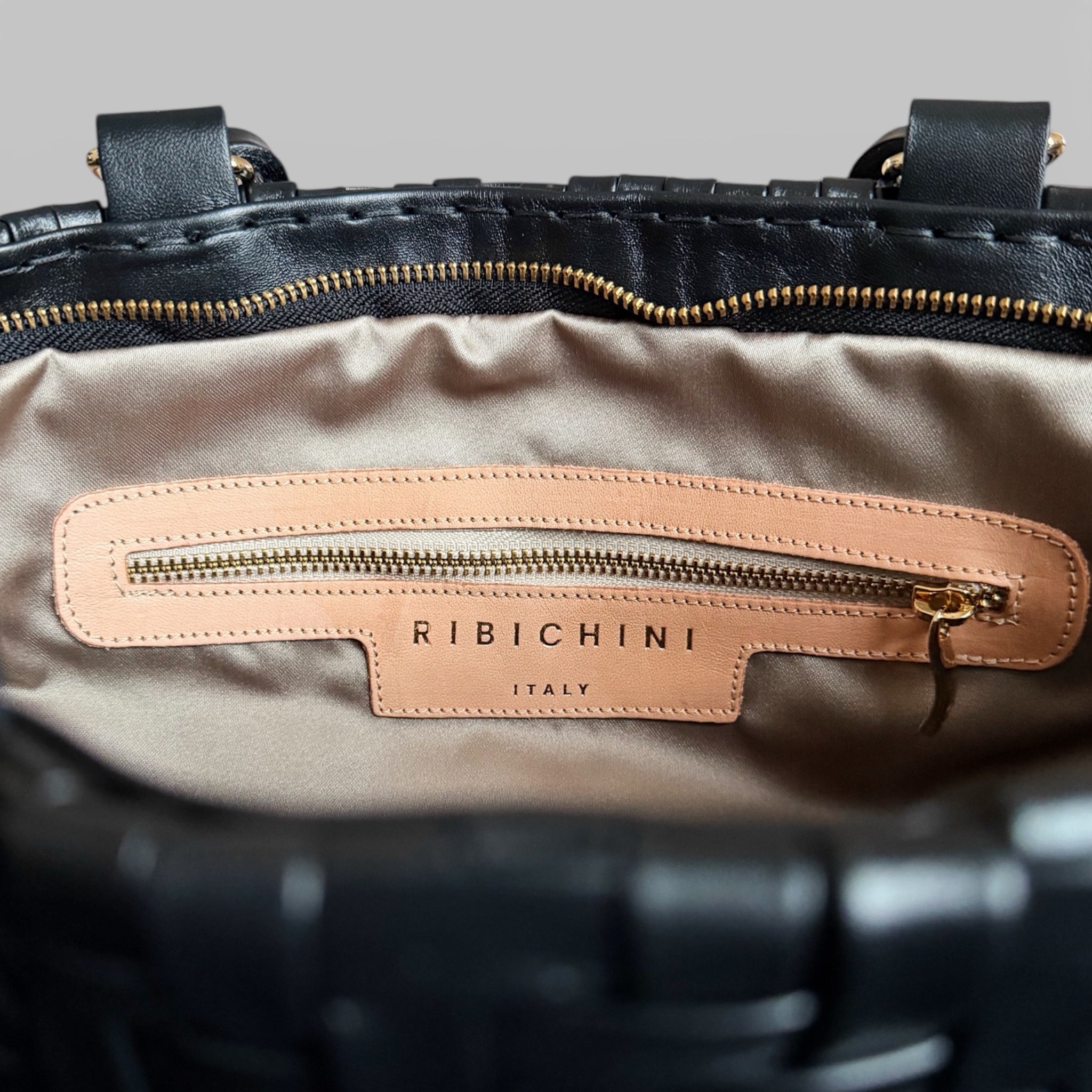 Bildet viser innsiden av en sort Ribichini Safari-veske, med en gullfarget glidelåslomme og merkets ikoniske R-logo.