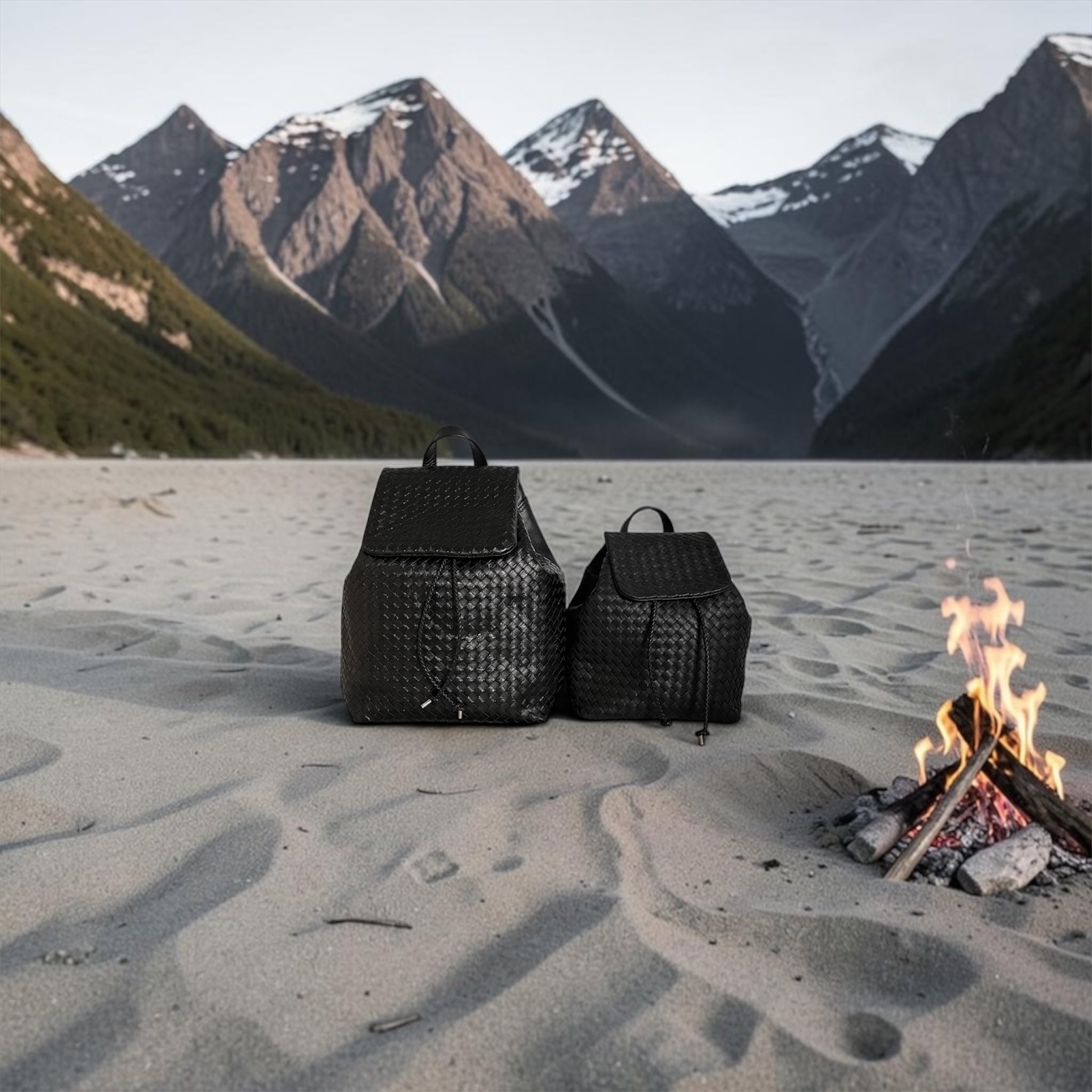 Ribichini Backpack Black håndflettet skinnsekk i sort skinn, fotografert på sandstrand med fjell, vann og bål i bakgrunnen.
