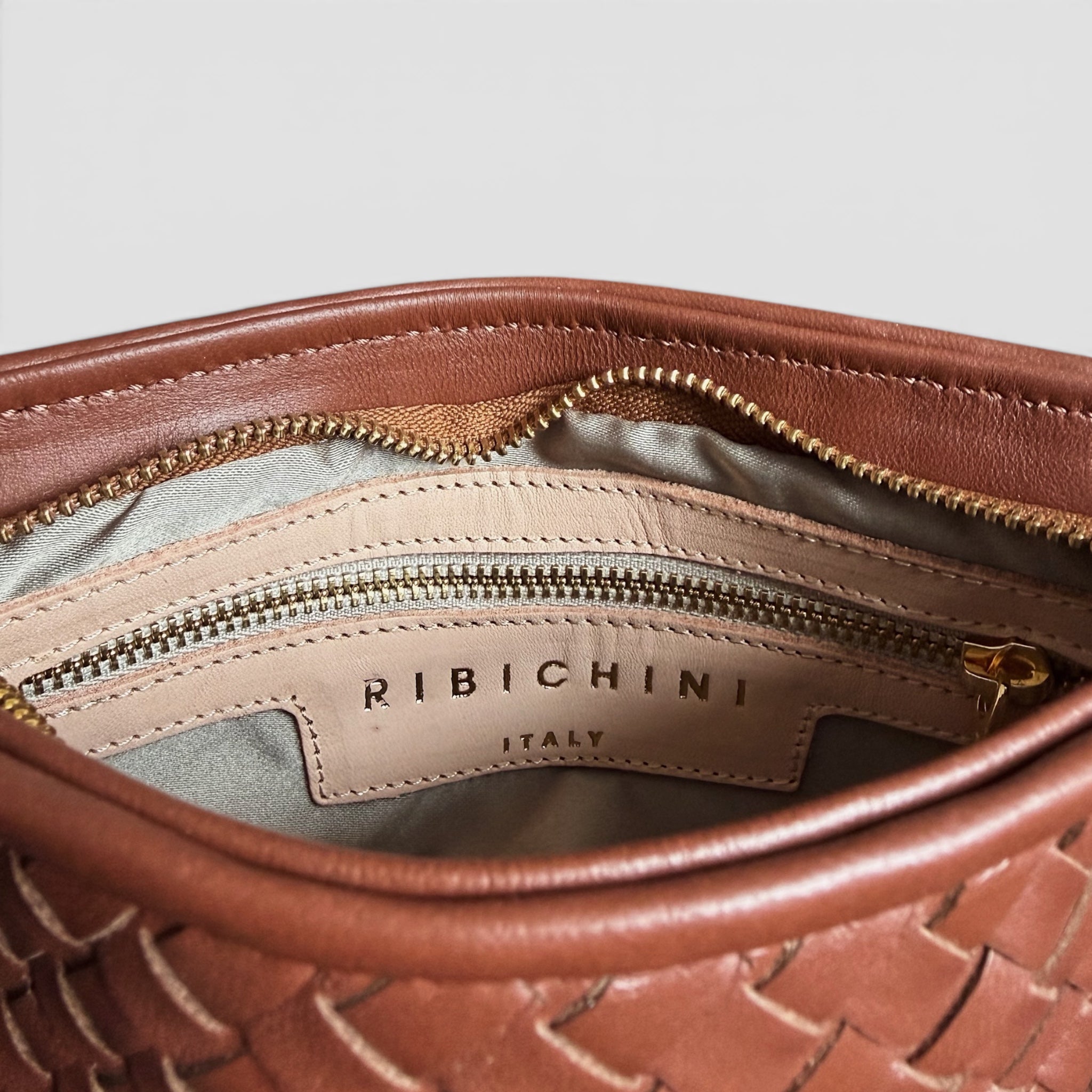 Innside av Ribichini Camper Clean Clutch Bruciato med glidelås, innerlomme og logodetalj i håndflettet lammeskinn.