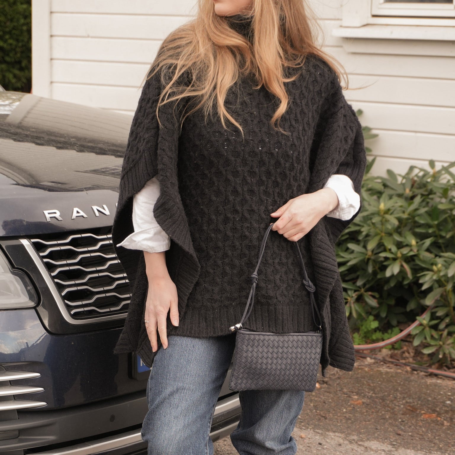 Ribichini Camper Clean Clutch Navy håndflettet skinnveske med skulderrem, båret med sort strikk, jeans og brune støvler.