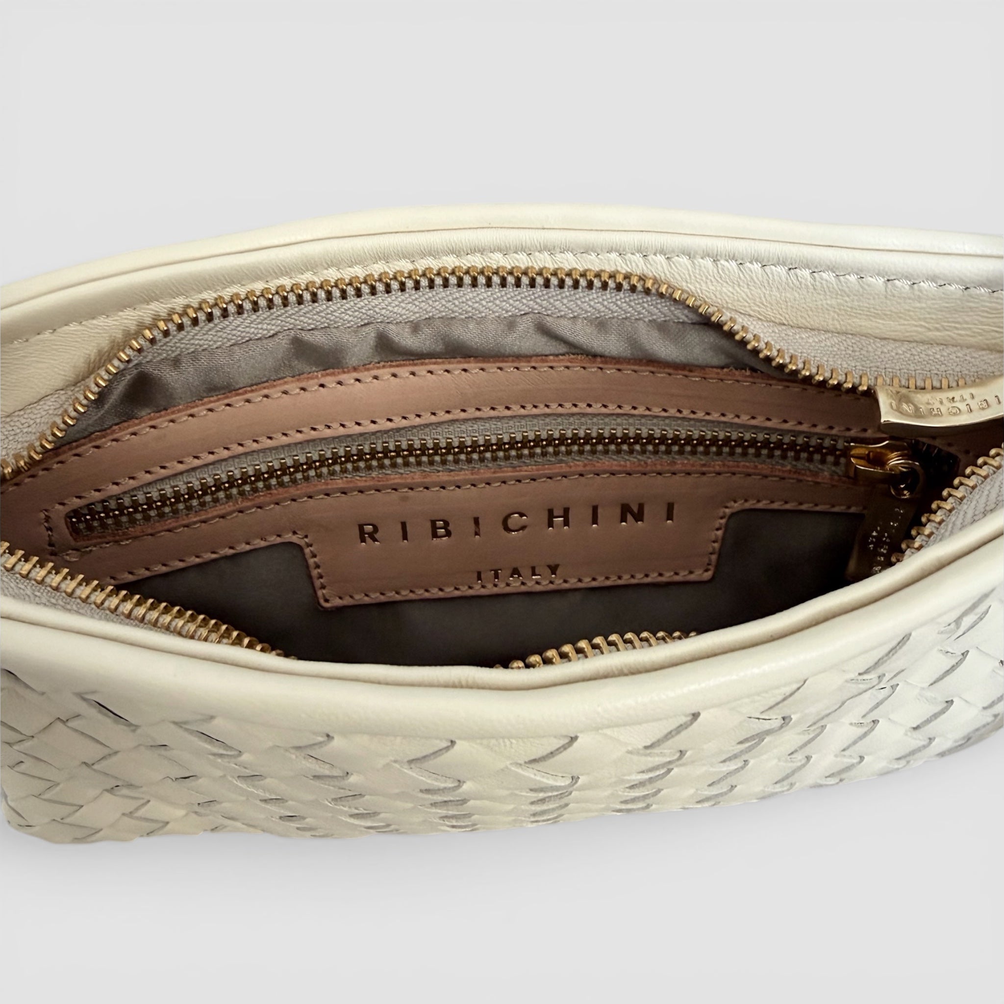 Ribichini Camper Clean Clutch Cream i håndflettet creamfarget lammeskinn med justerbar skulderrem og gulldetaljer.