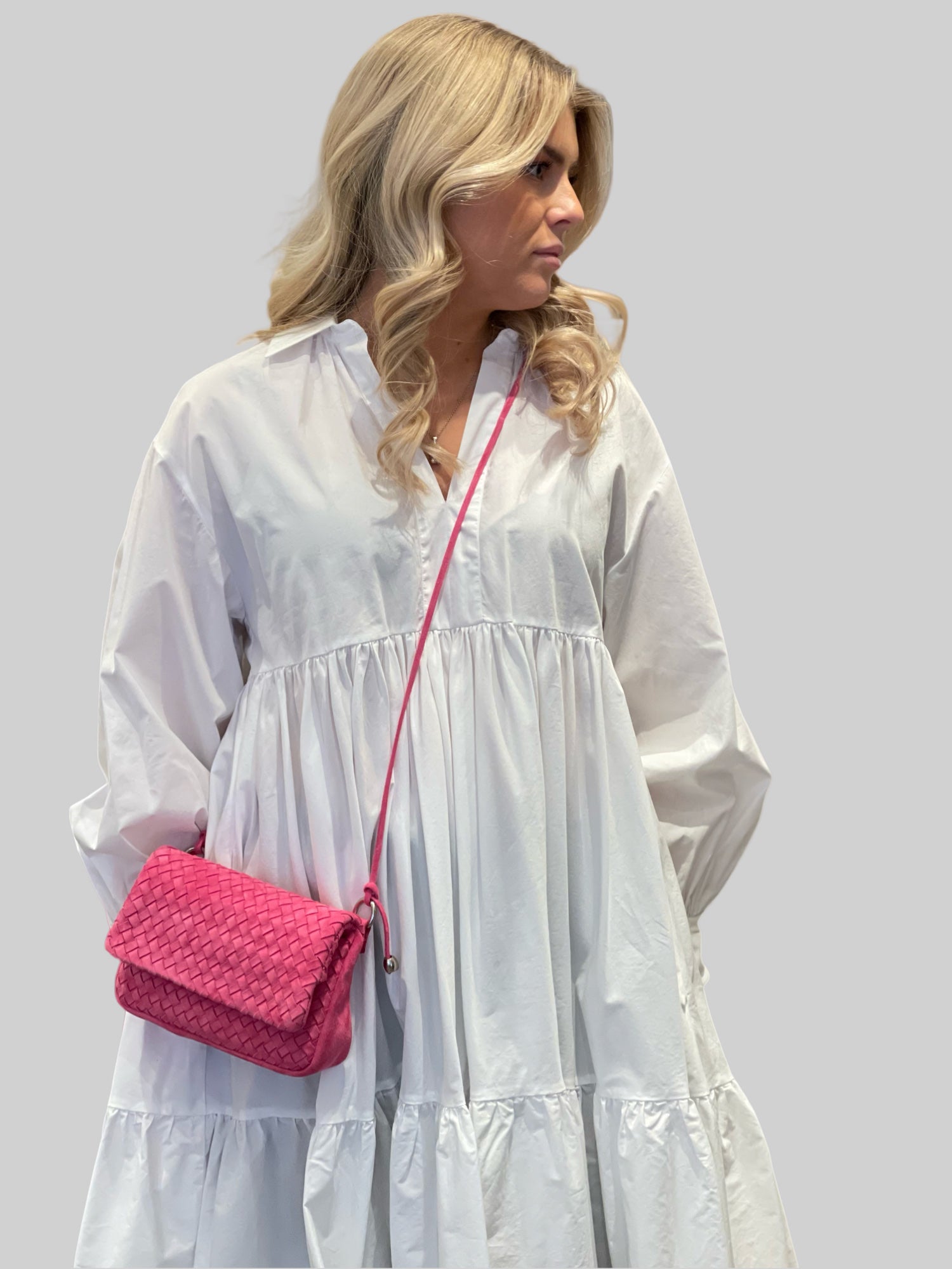 En ung kvinne i hvit kjole bærer stolt en Ribichini Undercover skinnveske i rosa. Vesken, laget av semsket flettet skinn, tilfører en trendy og sofistikert stil til antrekket hennes.