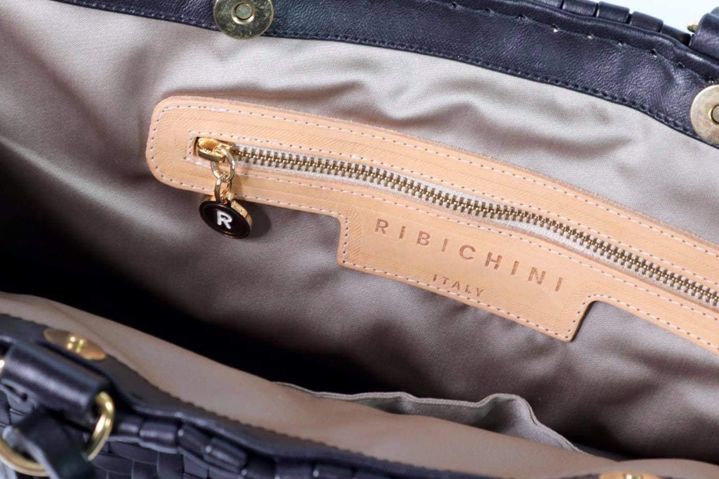 Bildet viser innsiden av en sort Ribichini Safari-veske, med en gullfarget glidelåslomme og merkets ikoniske R-logo, som kombinerer praktisk design med elegant detaljering.