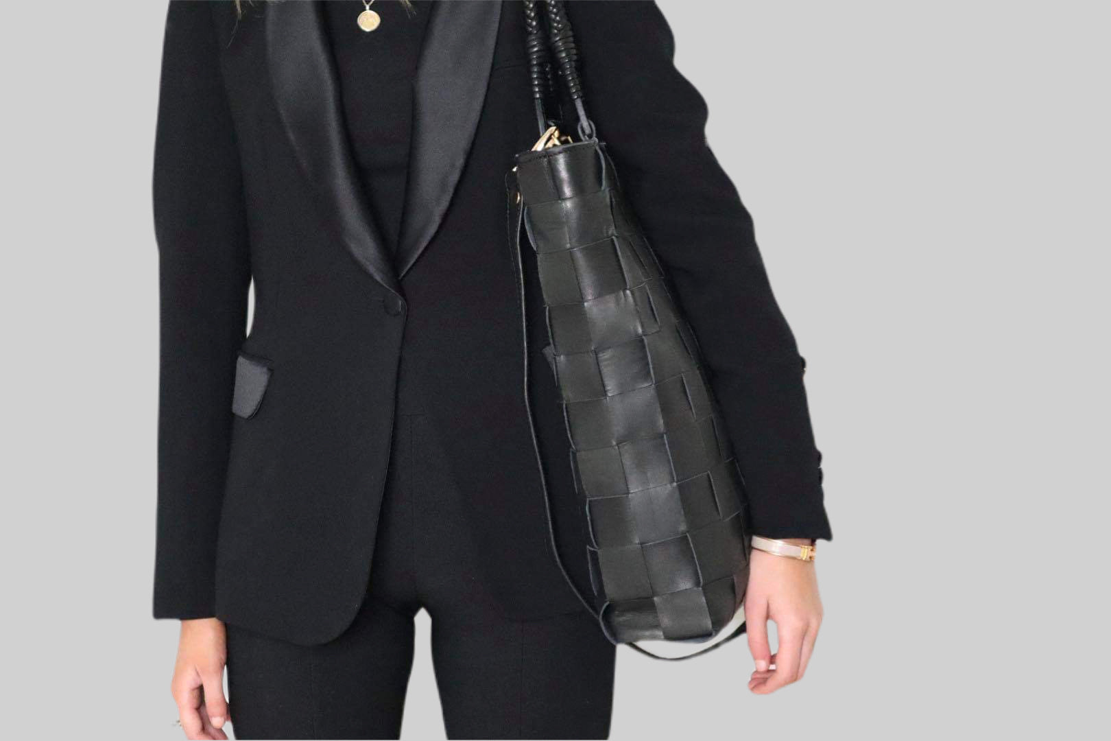 En elegant ung kvinne i sort dress bærer en Ribichini Square skinnveske over skulderen. Vesken, sett fra fronten, viser detaljene og designen tydelig.