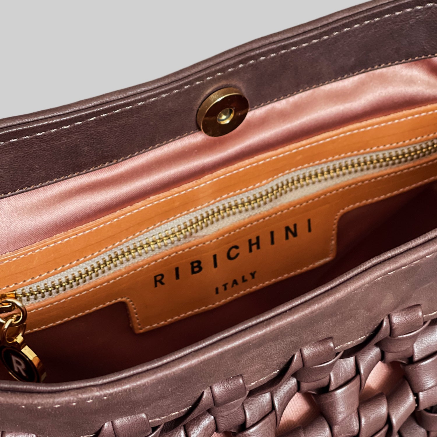 Innsiden av Ribichini Donna-vesken har et silkemykt, lysrosa fôr og en elegant lærpatch med "RIBICHINI ITALY" i gullskrift. En praktisk glidelåslomme med gyllen glidelås legger til funksjonalitet.