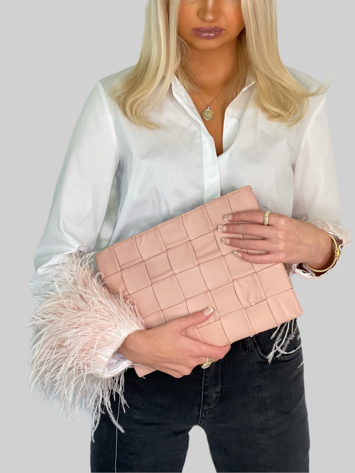 Ung kvinne i hvit skjorte med rosa detaljer bærer Ribichini Square Clutch i rosa. Perfekt match med sitt myke lammeskinn og flettemønster.