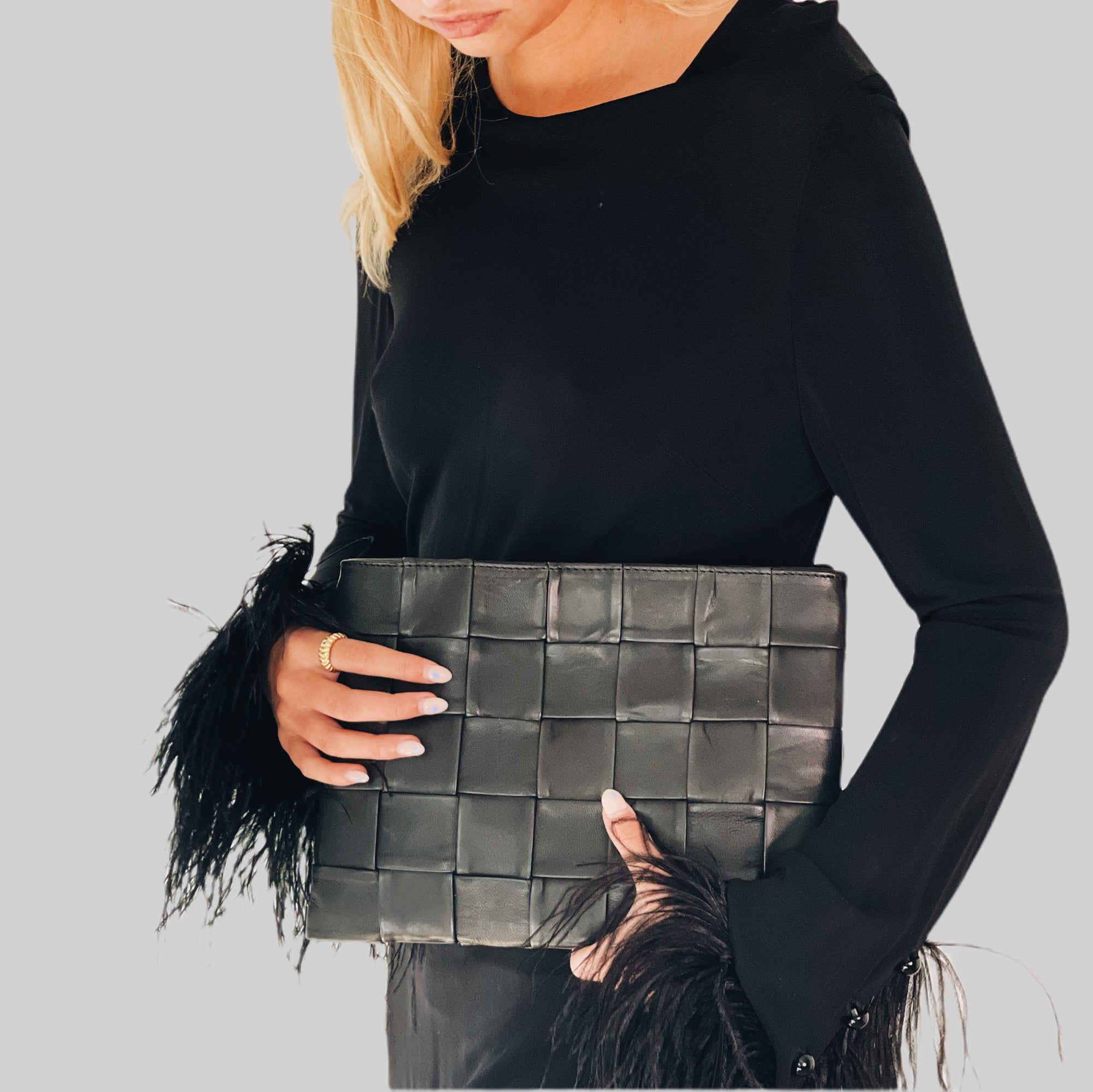 En stilig ung kvinne i sort kjole med strutsefjær, bærer en elegant Ribichini Square Clutch i sort, som tilfører sofistikert preg til antrekket hennes.