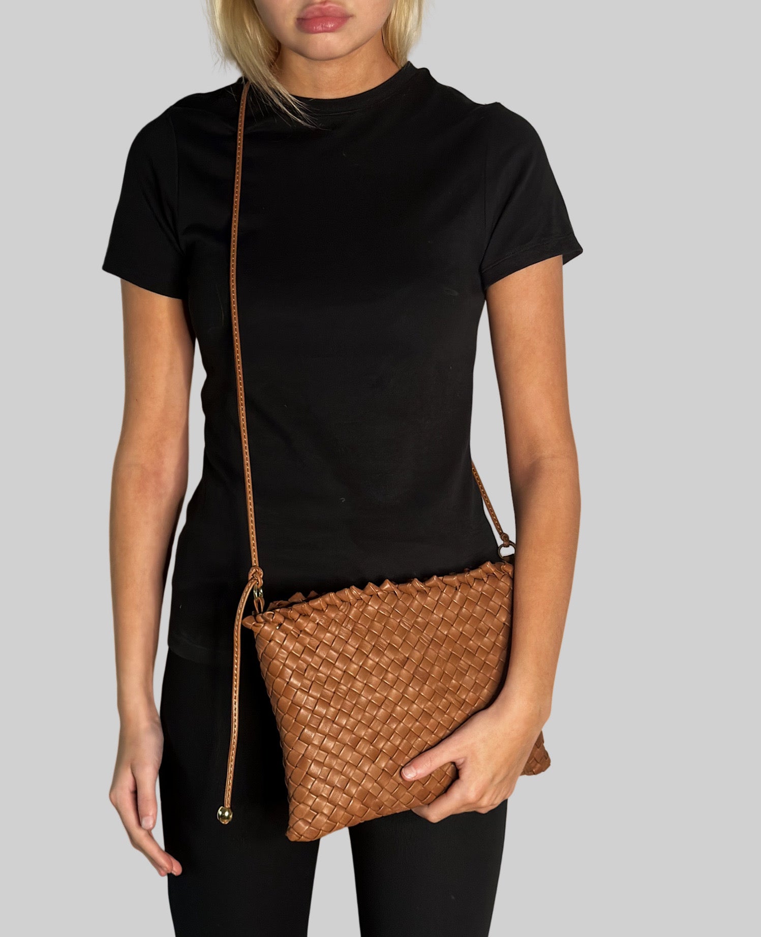 Ung kvinne i sort antrekk bærer en cognac Ribichini Woodstock-clutch med flettet design og slank skulderrem.