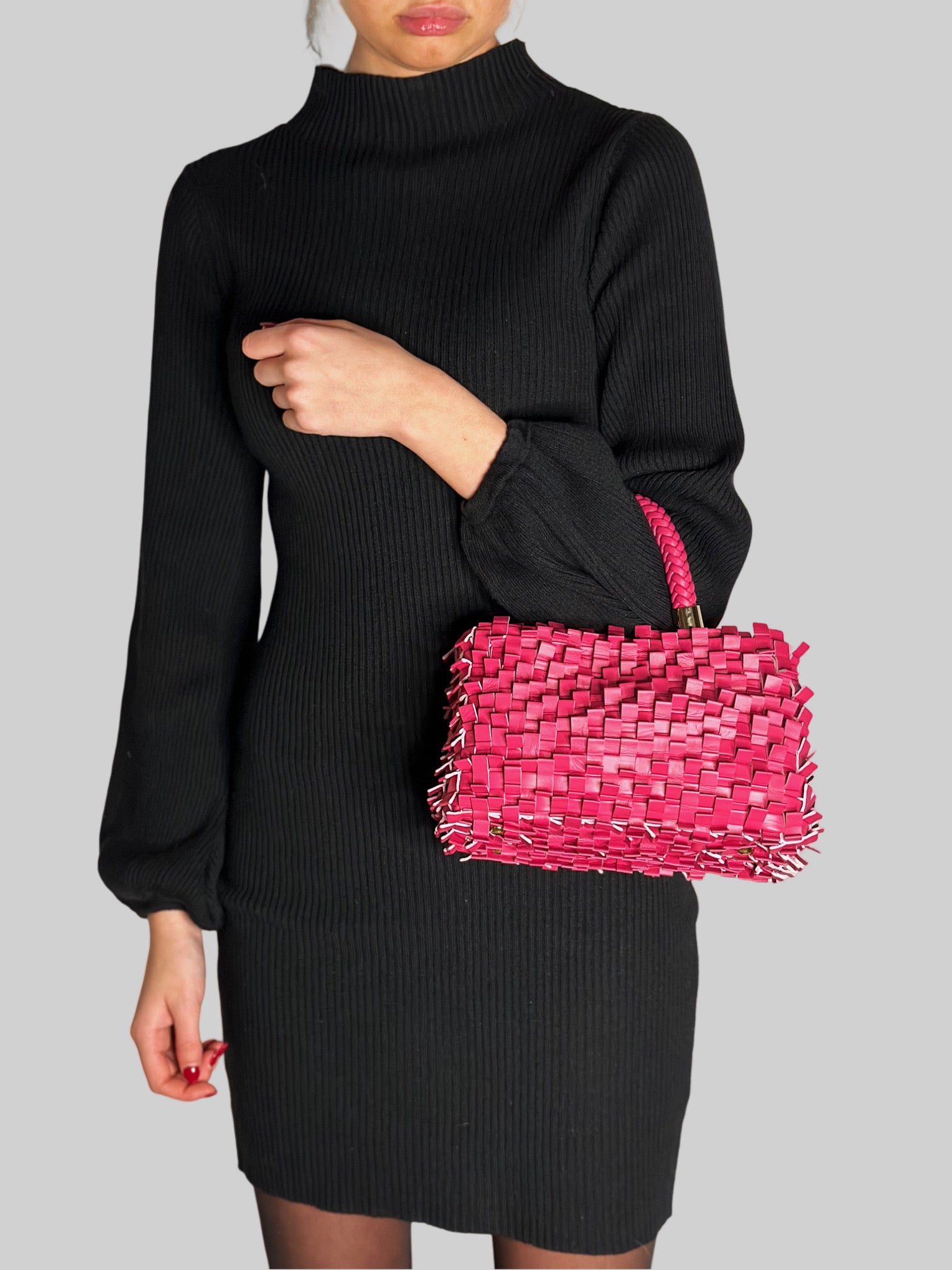 En ung kvinne i sort kjole stråler med en iøynefallende rosa Ribimini-veske, et elegant valg som tiltrekker oppmerksomhet.